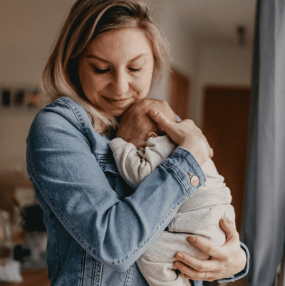 Zufriedene Kundin zum Life Coaching von junger Mutter mit Baby auf dem Arm zum Thema Vereinbarkeit von Karriere und Familie nach der Elternzeit