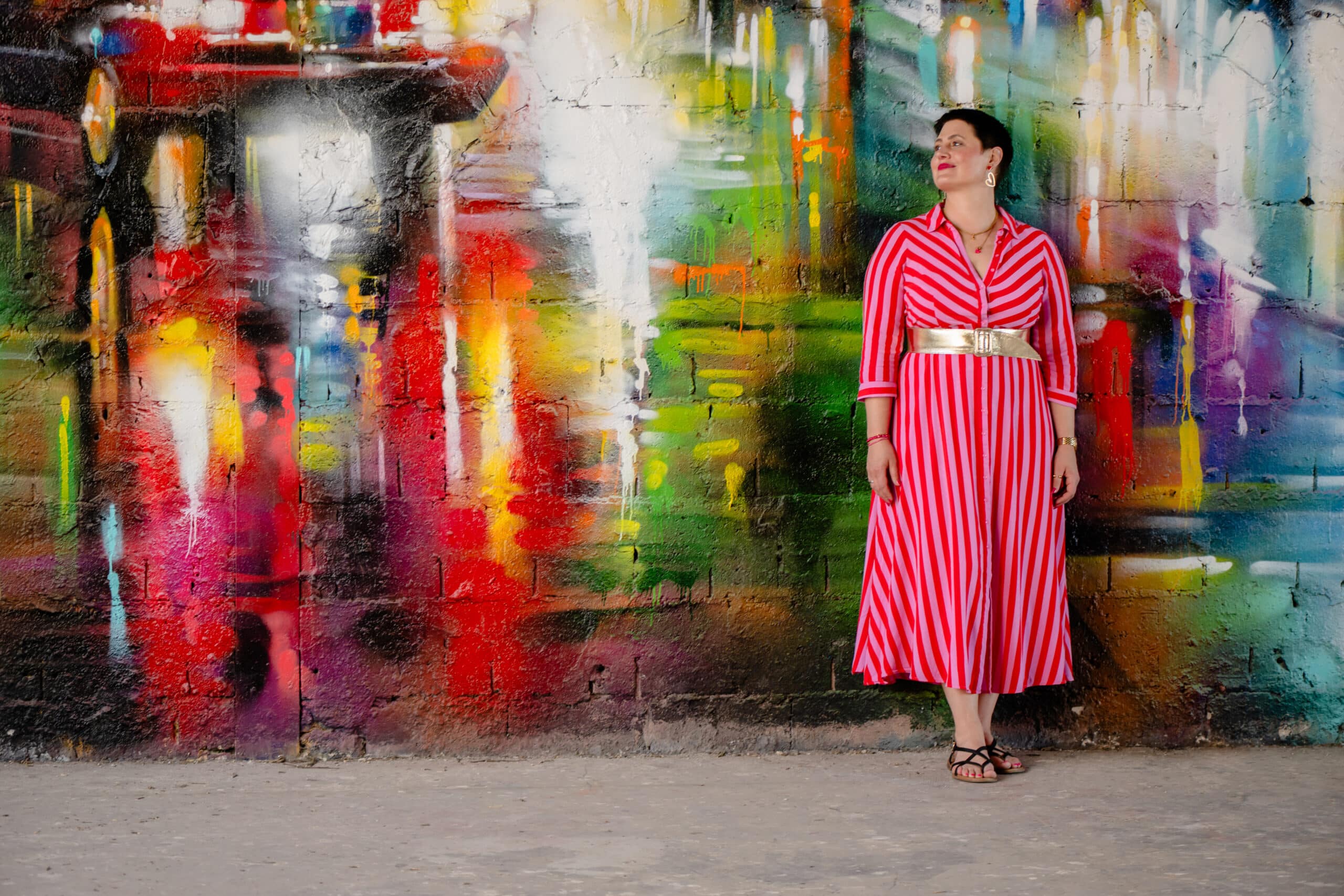 Coachin Luisa Riffel steht in einem rot-weiß gestreiften Kleid vor einer farbenfrohen Graffiti-Wand in Berlin auf dem Teufelsberg.