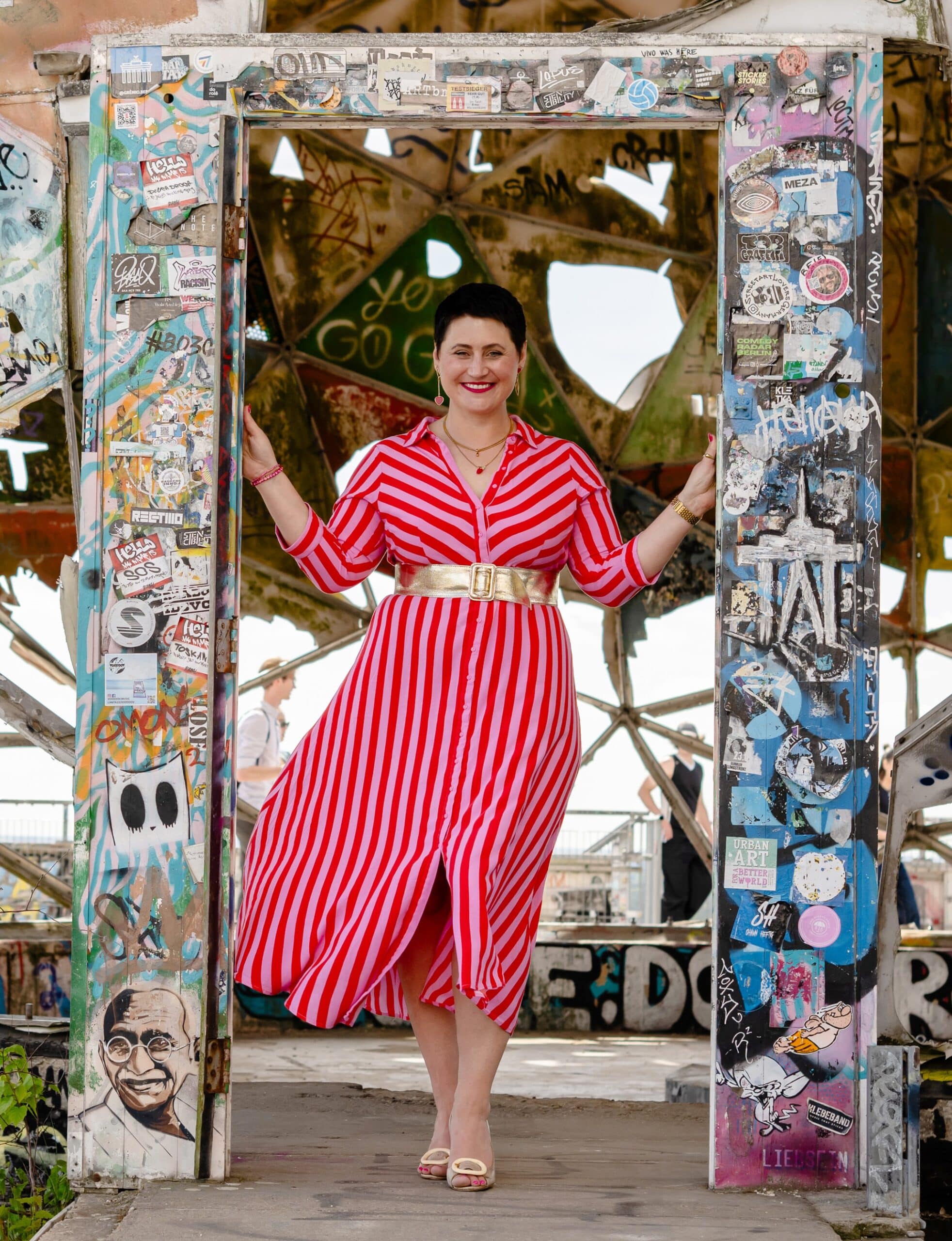 Coachin Luisa Riffel tritt lächelnd durch eine bunt beklebte Tür auf dem Berliner Teufelsberg – ein Bild für Neuanfang, Selbstführung und mutige Veränderung.