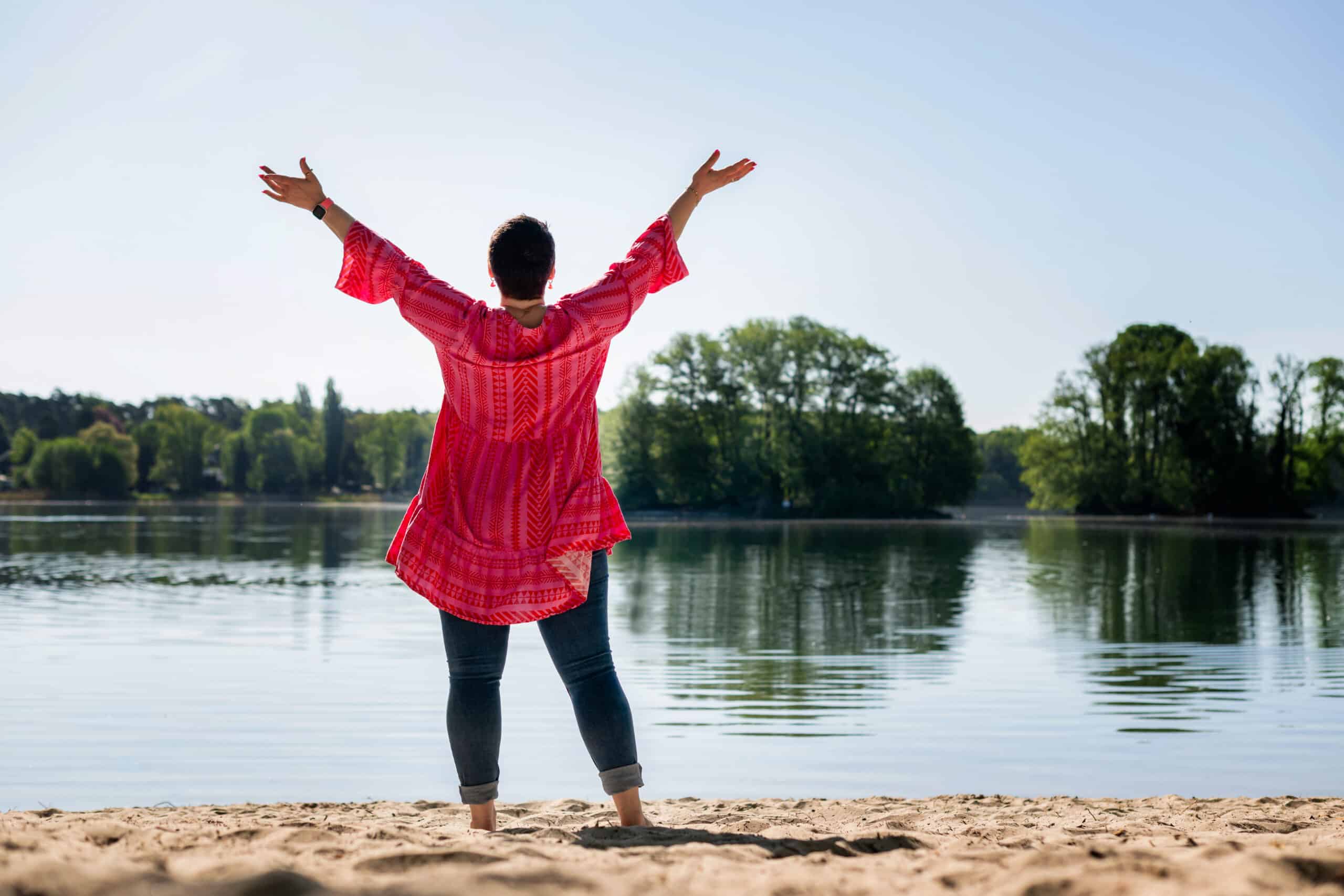 Luisa Riffel steht am See mit offenen Armen – Coaching für Frauen in Berlin und versprüht Selbstbewusstsein und Lebensfreude